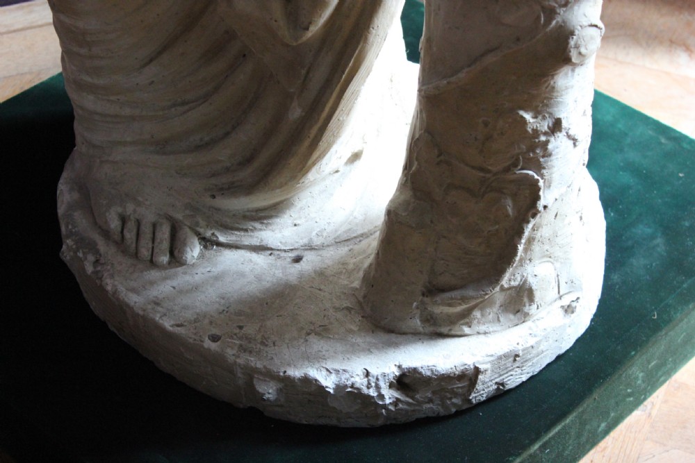 A full-length off-white plaster statue depicting a classical draped female figure standing beside a pedestal basin. View XII