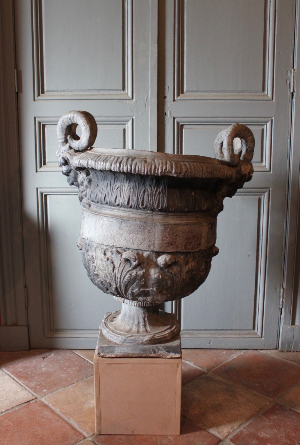 A large 18th-century cast lead urn featuring scrolled handles, relief leaf decoration, and a square base.