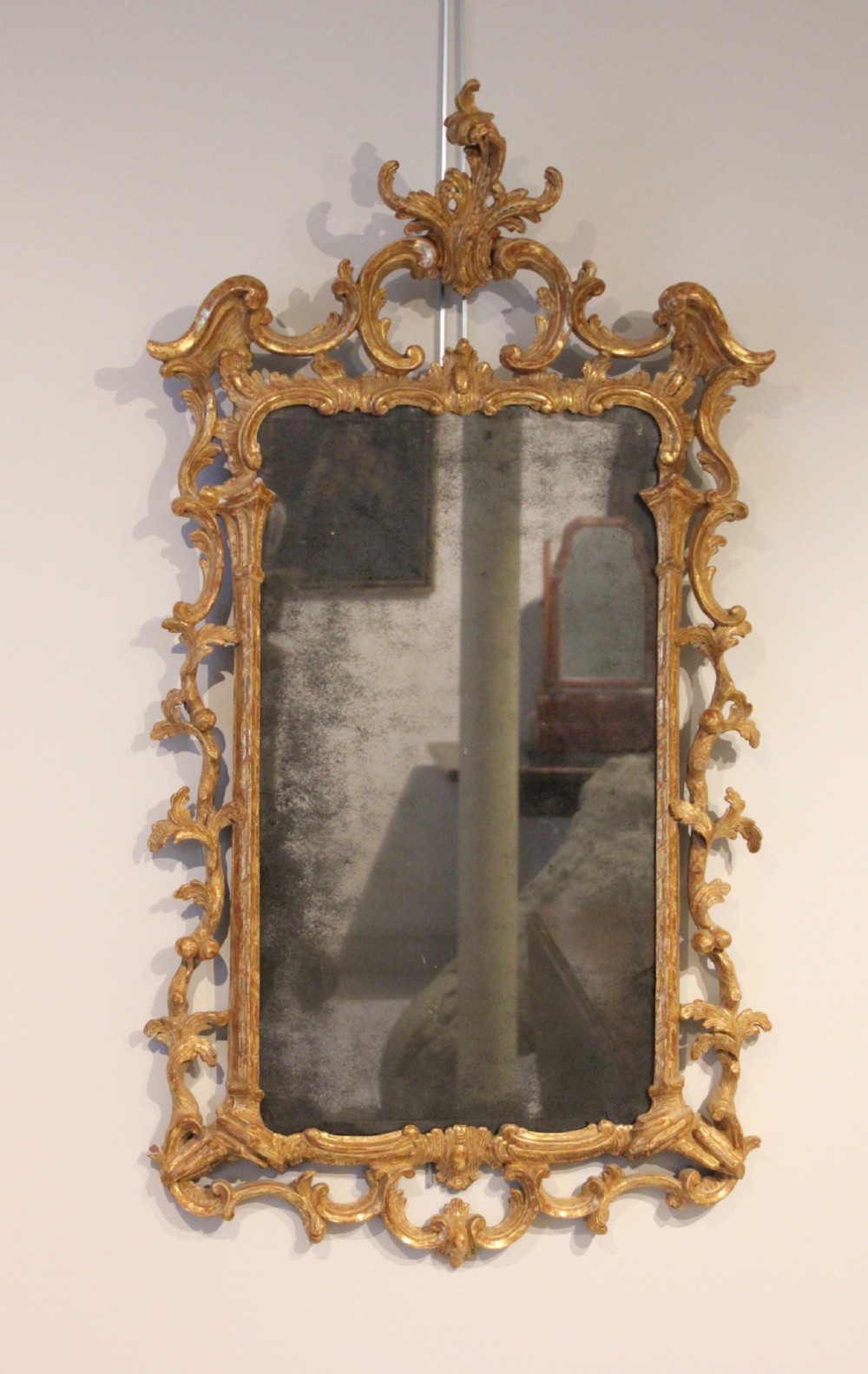 An 18th-century English Rococo wall mirror featuring an intricate carved giltwood frame with C-scrolls and acanthus foliage surrounding an aged glass plate.