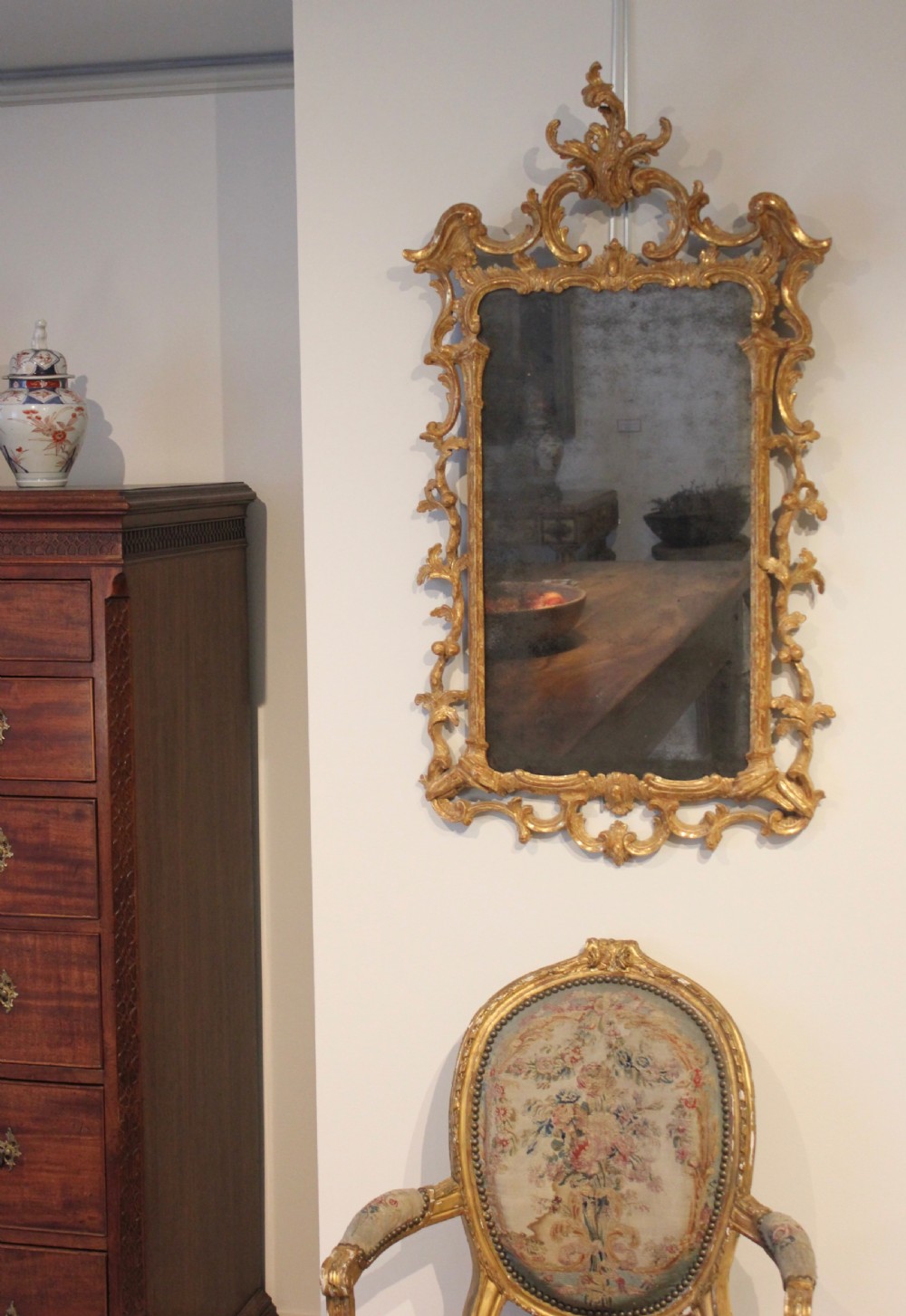 An 18th-century English Rococo wall mirror featuring an intricate carved giltwood frame with C-scrolls and acanthus foliage surrounding an aged glass plate. View II
