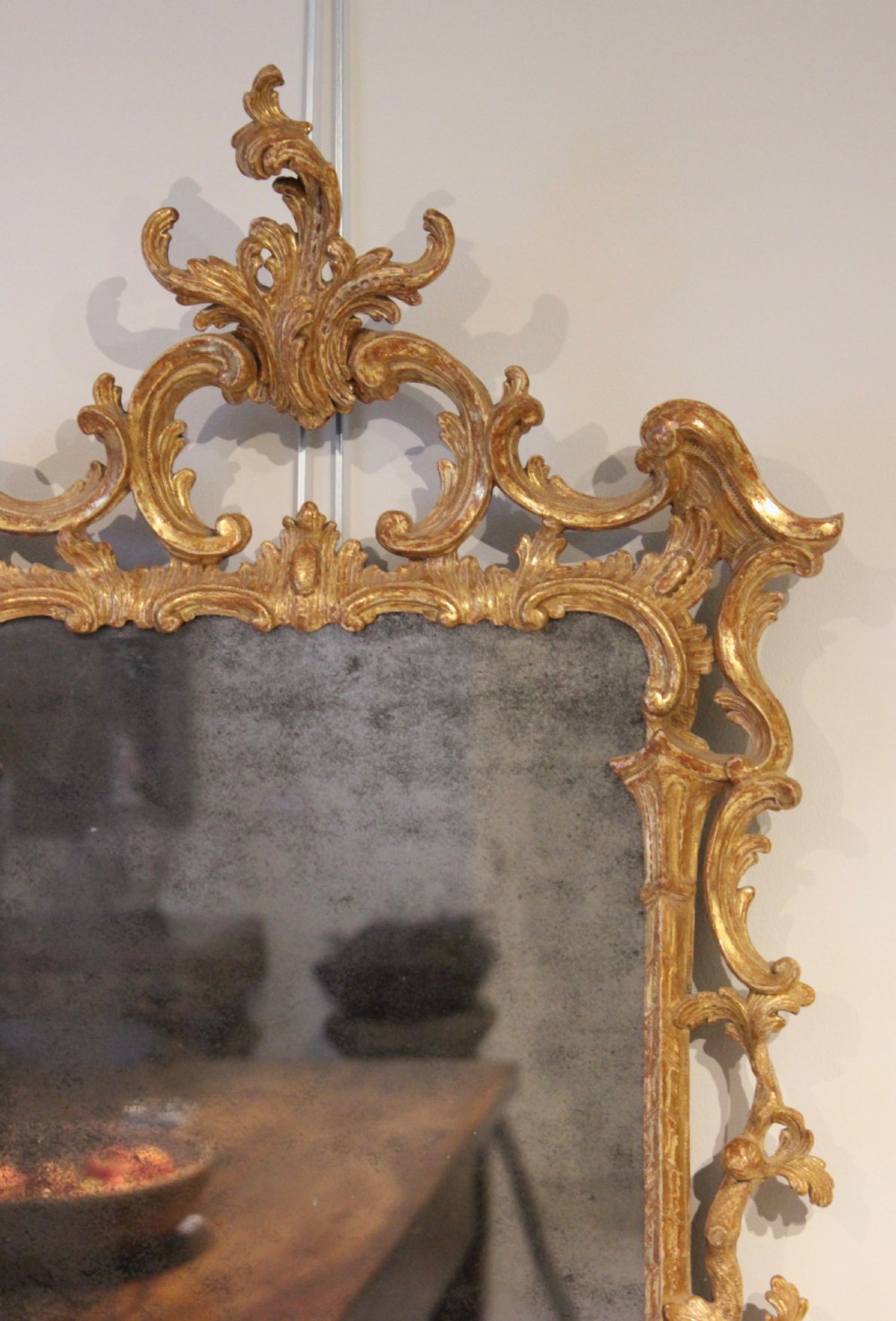 An 18th-century English Rococo wall mirror featuring an intricate carved giltwood frame with C-scrolls and acanthus foliage surrounding an aged glass plate. View III