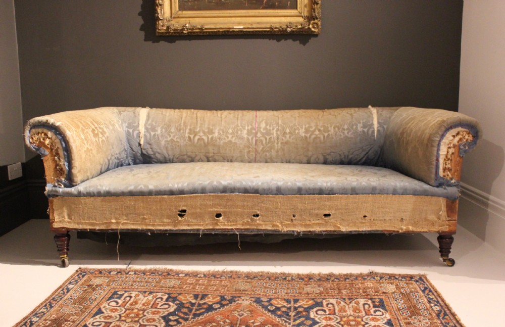 A Victorian Chesterfield sofa with rolled scroll arms, turned timber legs on brass castors, and patterned blue damask fabric over visible jute webbing. View II