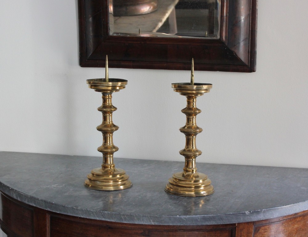 A pair of 16th-century brass pricket candlesticks featuring turned knopped stems and stepped circular bases. View II