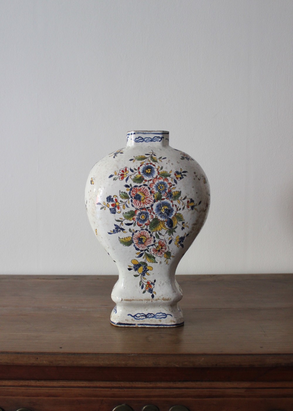 An eighteenth-century off-white tin-glazed ceramic vase decorated with hand-painted polychrome floral motifs across the front.