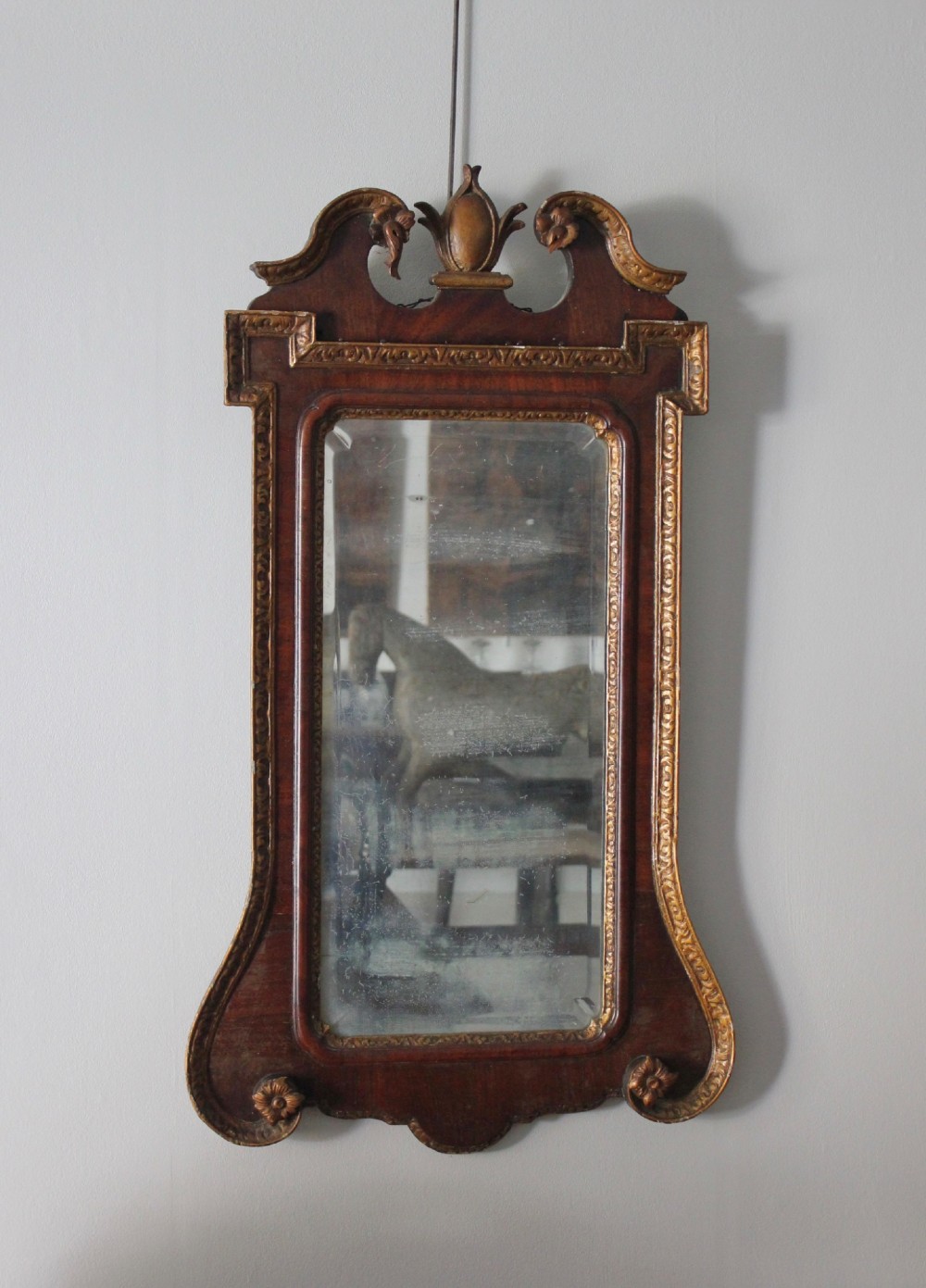 A mid-18th century Georgian mahogany wall mirror featuring a scrolled crested top with a gilded finial and carved slip moulding.