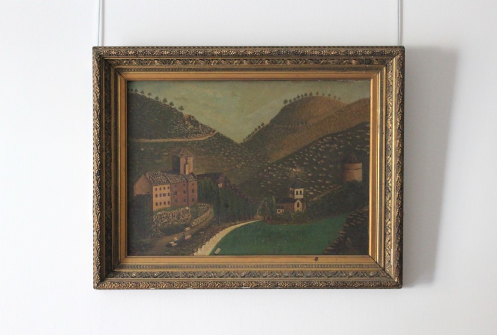 A 19th-century primitive oil painting depicting rolling hills, village buildings, and a winding path, housed in an ornate gilded frame. View II