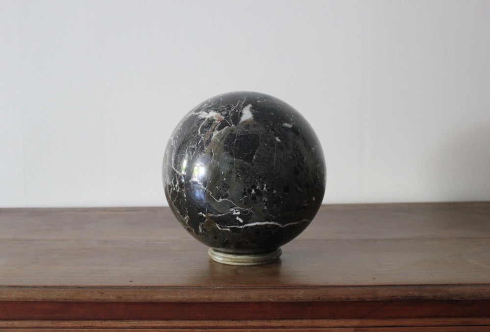 A large polished dark marble sphere featuring white and grey natural veining resting on a small circular stand.