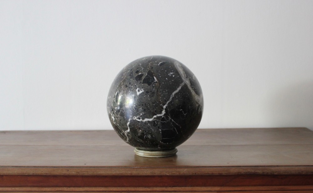 A large polished dark marble sphere featuring white and grey natural veining resting on a small circular stand. View II