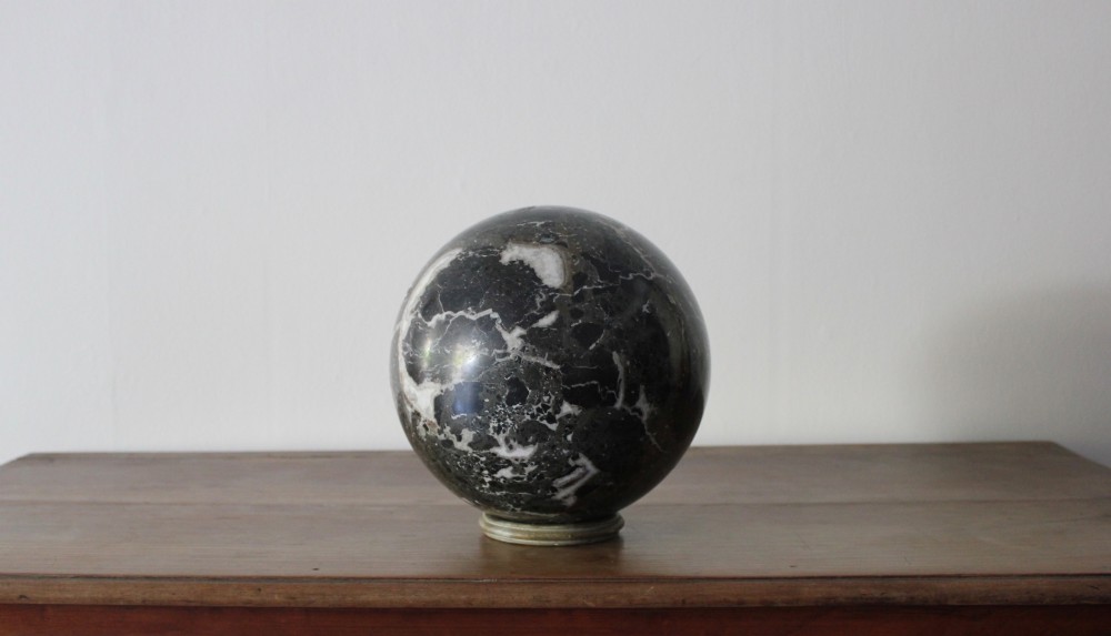 A large polished dark marble sphere featuring white and grey natural veining resting on a small circular stand. View III