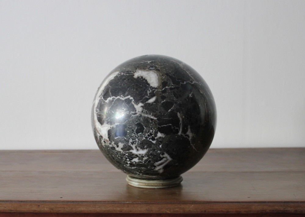 A large polished dark marble sphere featuring white and grey natural veining resting on a small circular stand. View IV