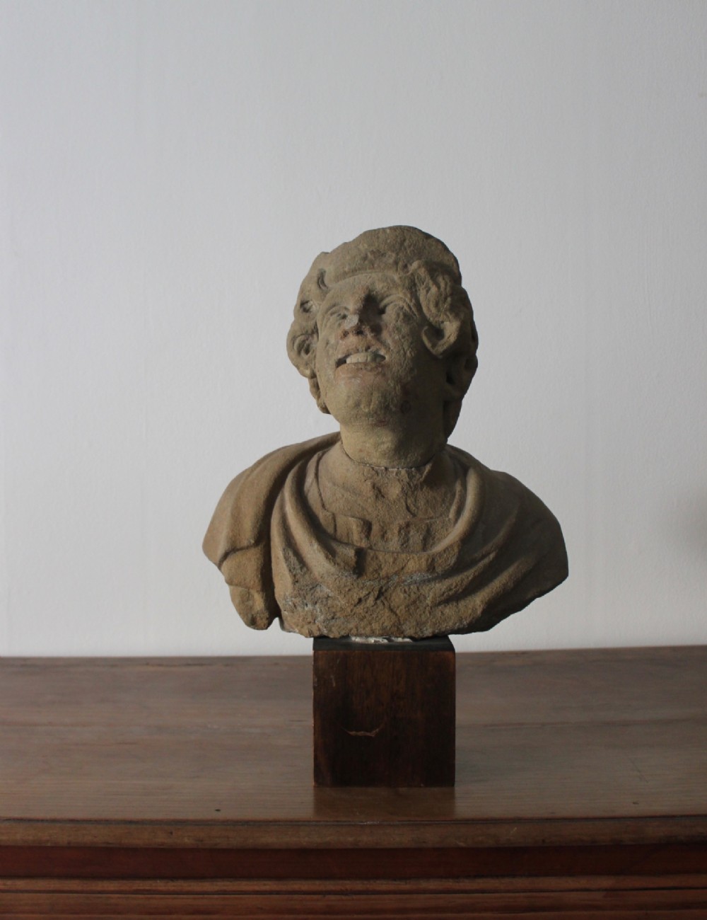 A hand-carved stone portrait bust depicting a figure looking upwards, mounted on a square wooden display block.