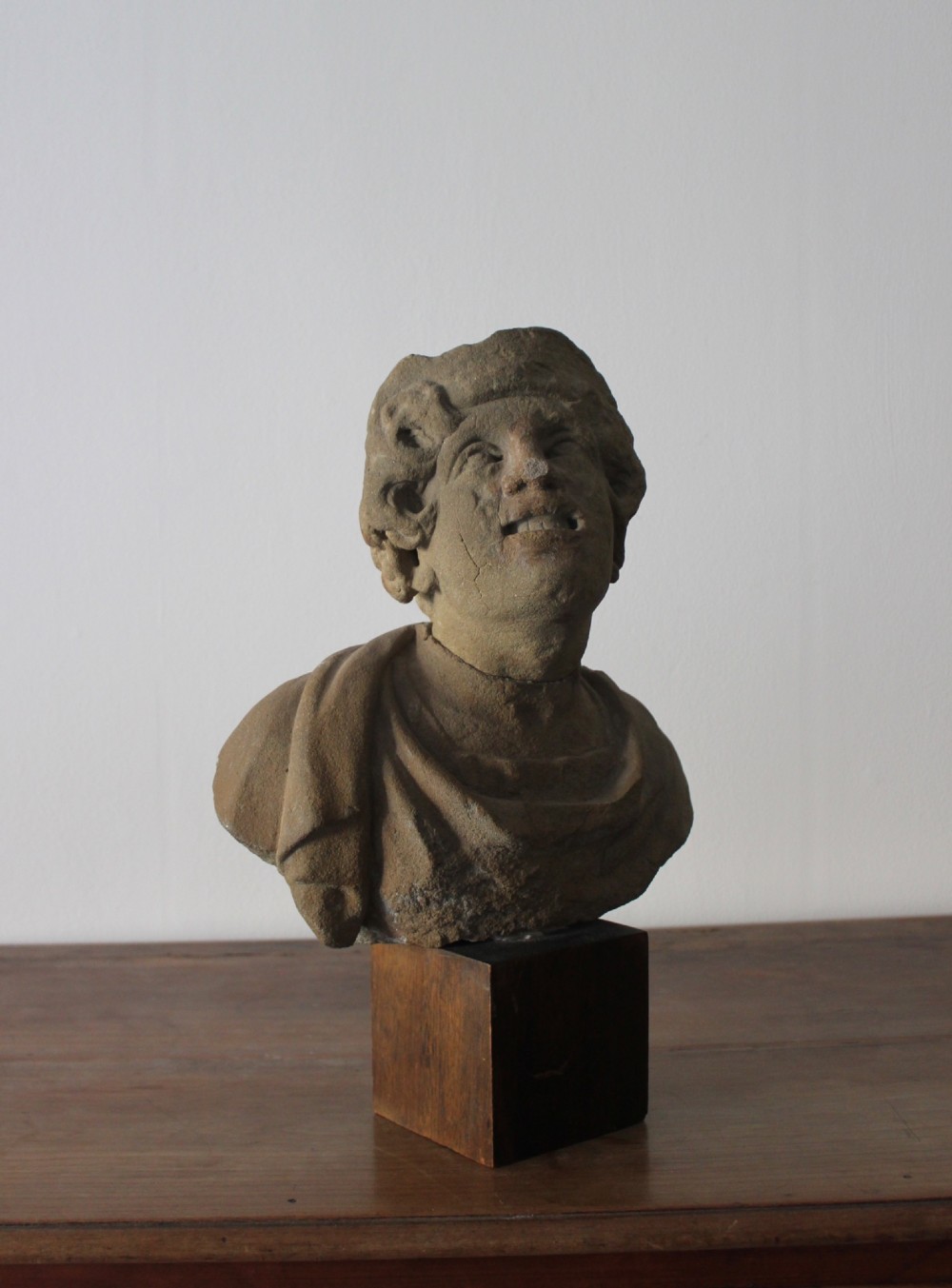 A hand-carved stone portrait bust depicting a figure looking upwards, mounted on a square wooden display block. View II