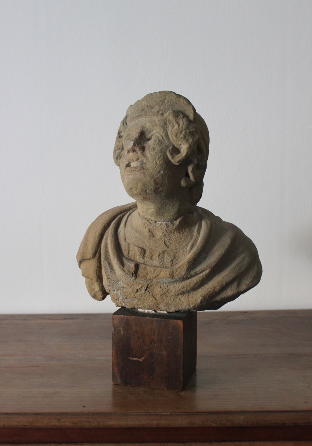 A hand-carved stone portrait bust depicting a figure looking upwards, mounted on a square wooden display block. View III