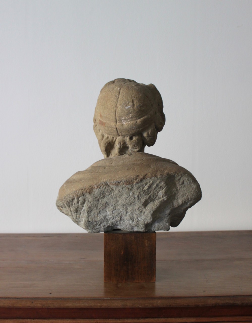 A hand-carved stone portrait bust depicting a figure looking upwards, mounted on a square wooden display block. View IV
