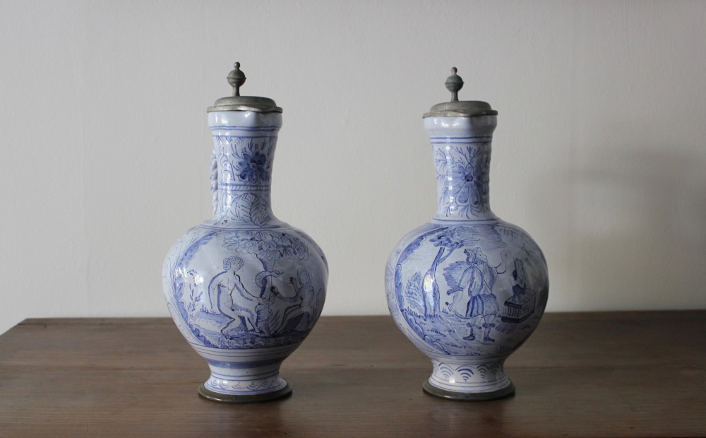 A matched pair of tin-glazed blue and white earthenware ewers featuring pewter hinged lids and twisted handles. View II