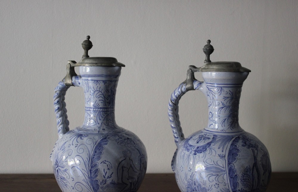 A matched pair of tin-glazed blue and white earthenware ewers featuring pewter hinged lids and twisted handles. View V
