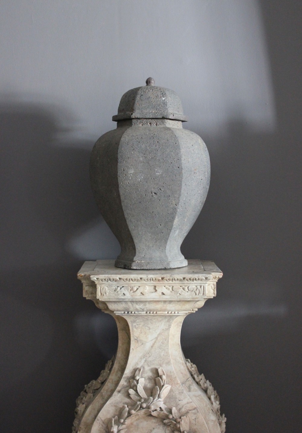 A large grey terracotta lidded urn with a faceted baluster body and textured finish.