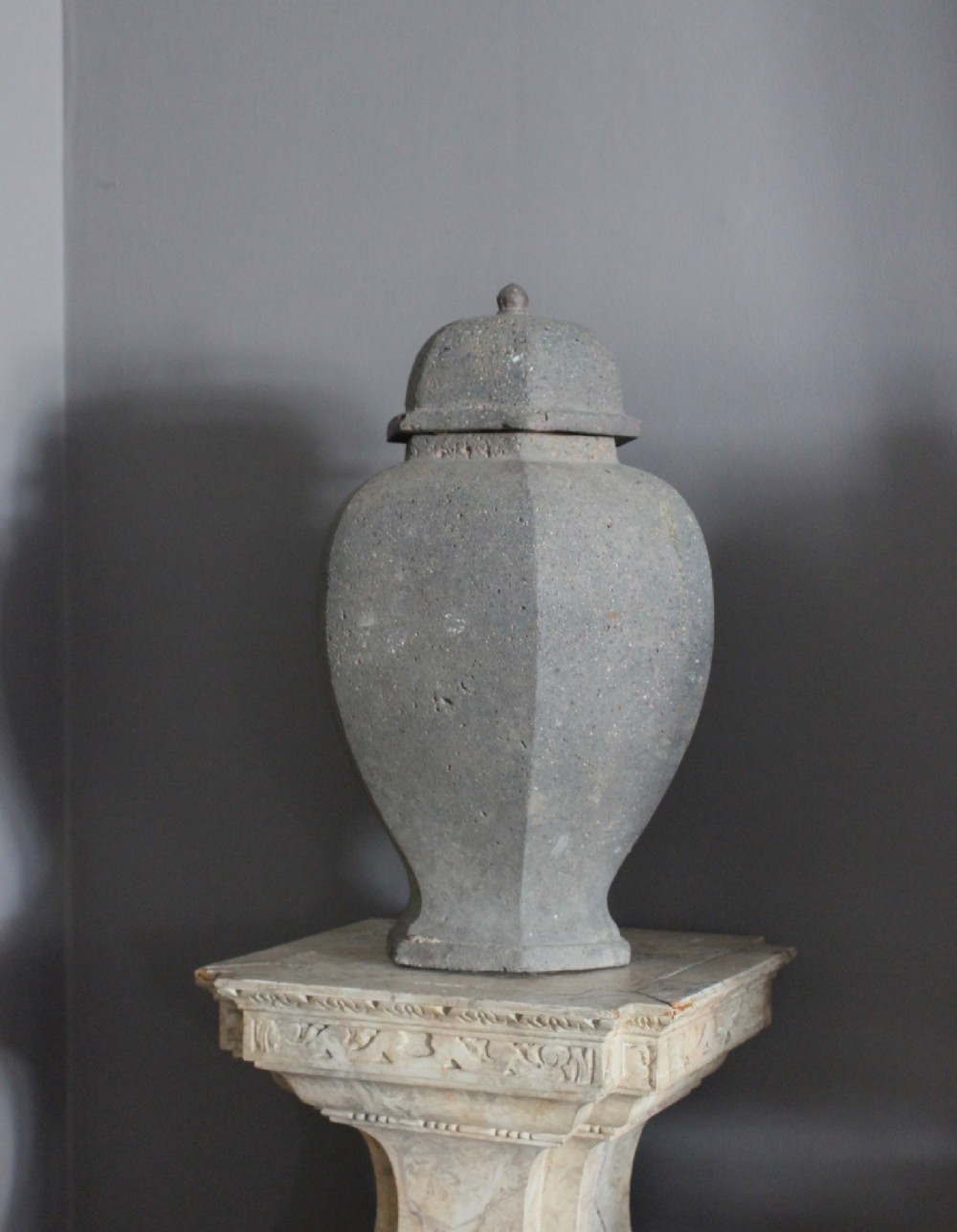 A large grey terracotta lidded urn with a faceted baluster body and textured finish. View V