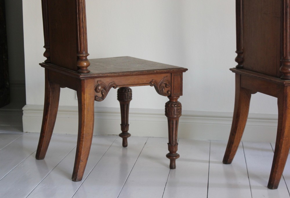 A pair of 19th-century English carved oak hall chairs featuring pediment backrests with central circular monograms and turned front legs. View IV