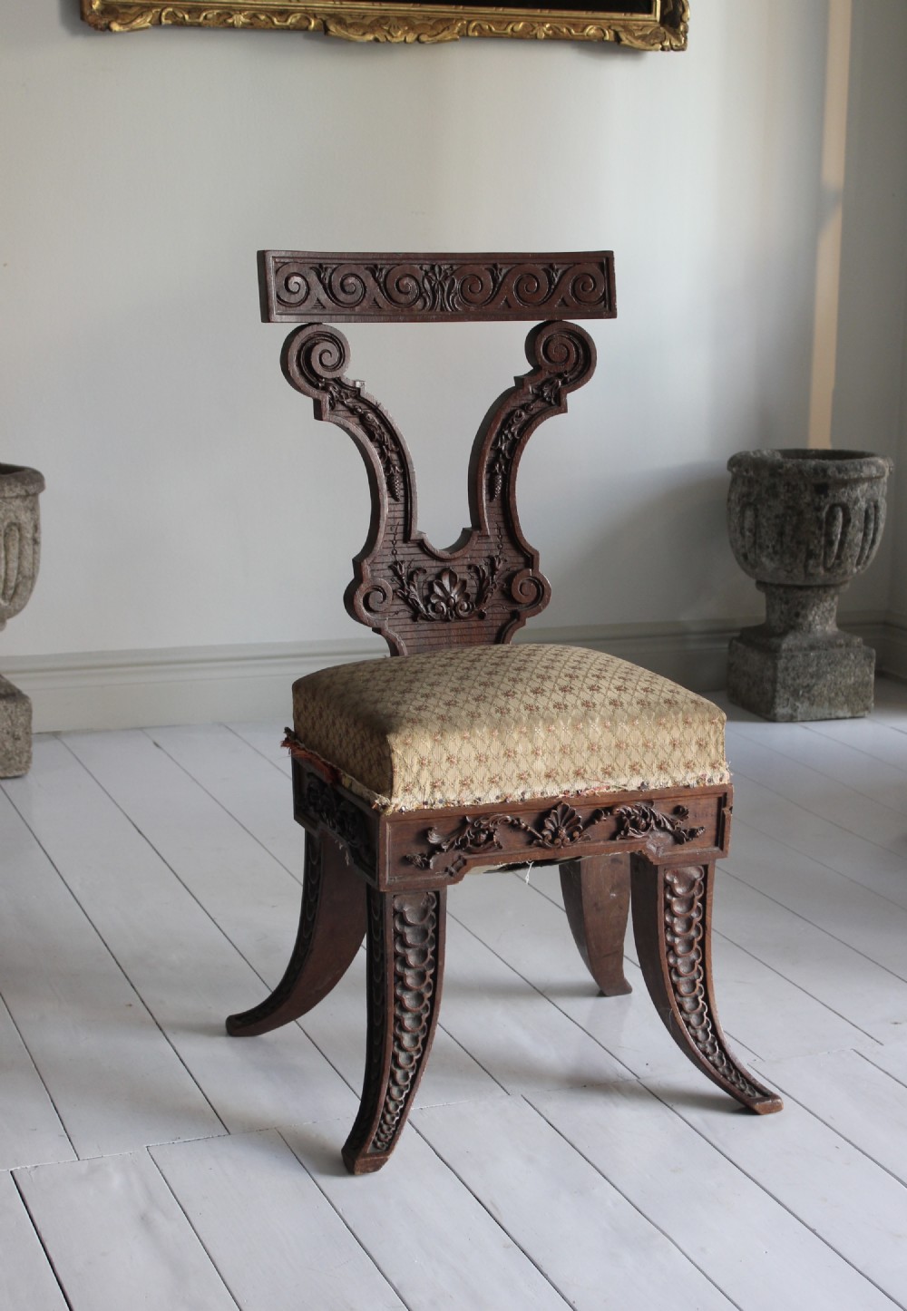 A dark carved wooden chair featuring a cello-shaped backrest, patterned fabric seat cushion, and carved curved legs.