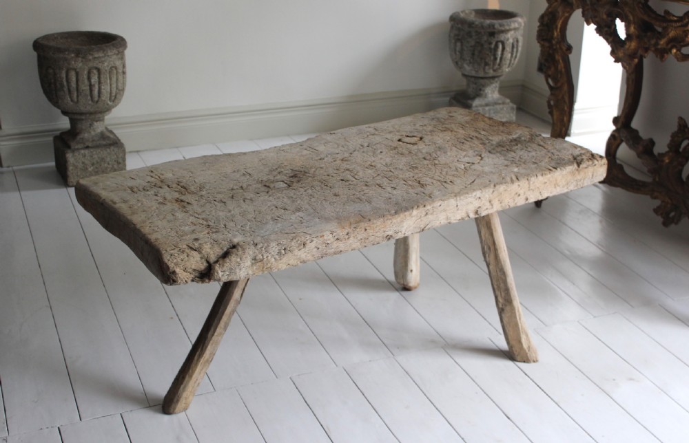 A low 18th-century primitive oak table featuring a thick, heavily weathered slab top resting on four organic, splayed wooden legs.