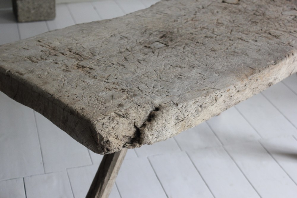 A low 18th-century primitive oak table featuring a thick, heavily weathered slab top resting on four organic, splayed wooden legs. View III