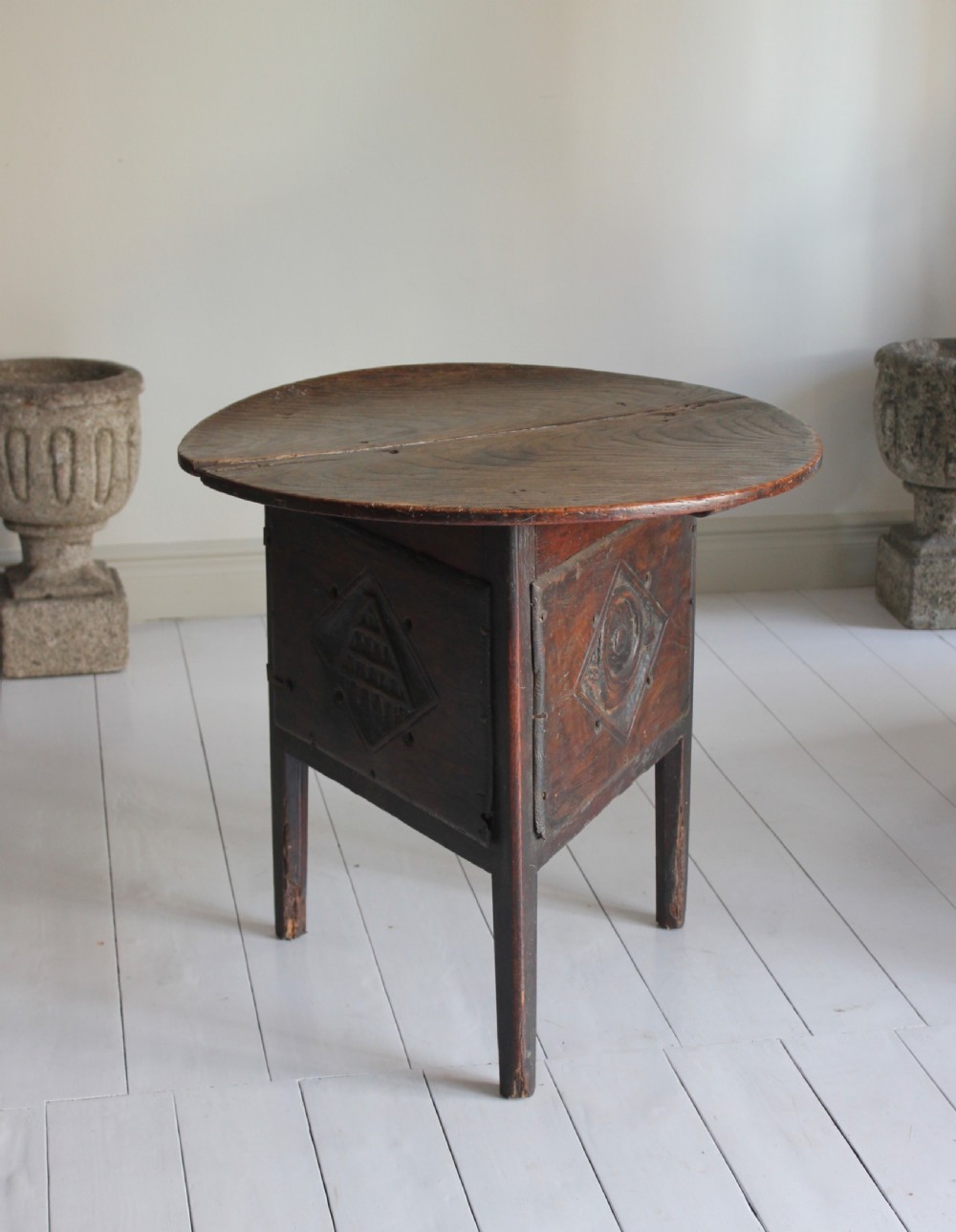 An 18th-century ash cricket table with a circular top resting on three legs and a carved geometric diamond panel frieze.
