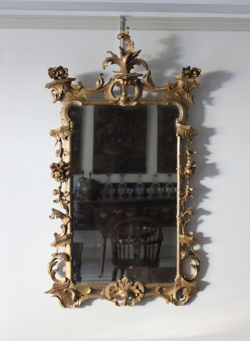 An 18th-century English Rococo rectangular wall mirror featuring an intricately carved gold giltwood frame with floral scrollwork and a decorative crest.