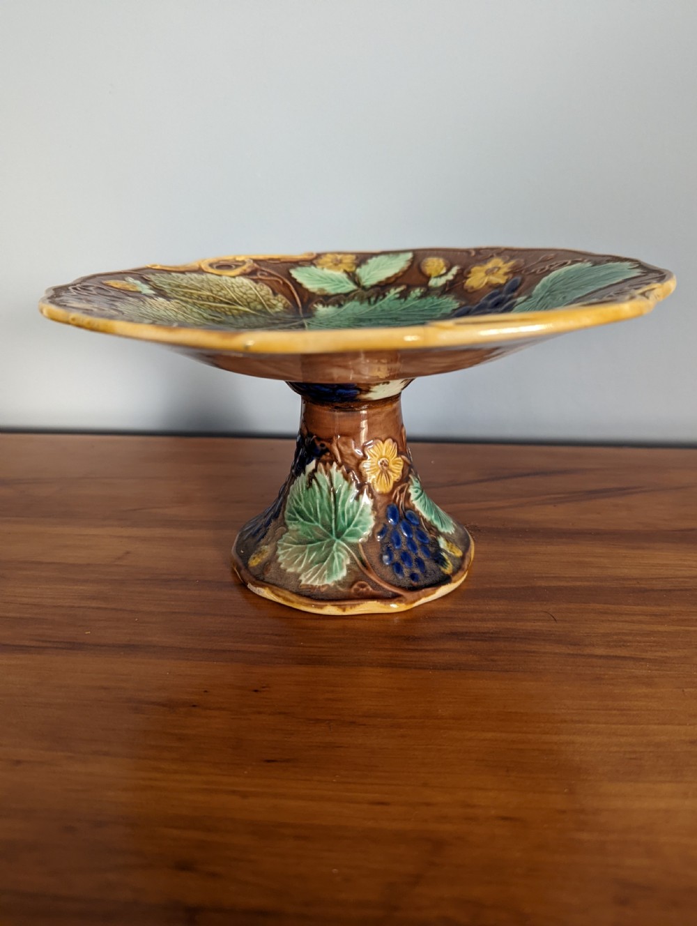 A Victorian majolica pedestal dish featuring moulded green leaves, blue berries, and yellow accents over a brown glazed earthenware surface. View III