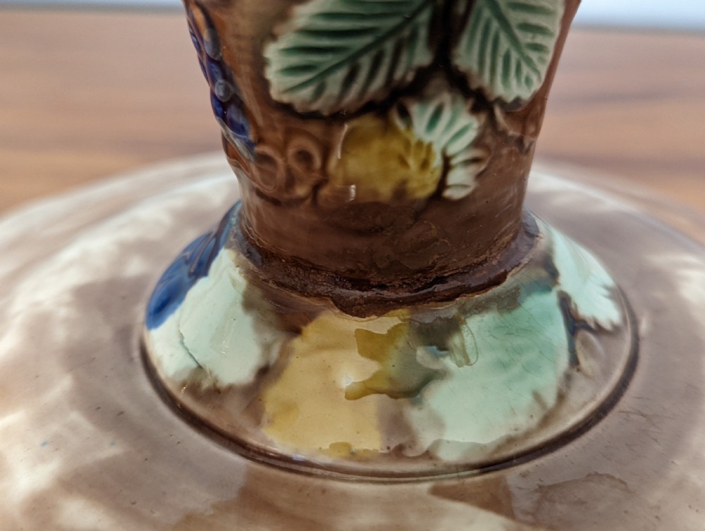 A Victorian majolica pedestal dish featuring moulded green leaves, blue berries, and yellow accents over a brown glazed earthenware surface. View V