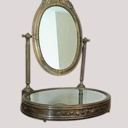 An antique French brass dressing mirror featuring a tilting oval frame with a ribbon crest, supported by fluted columns above a mirrored base. View II