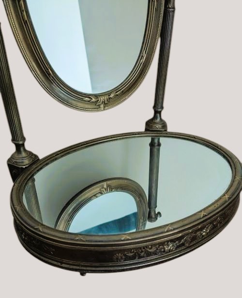 An antique French brass dressing mirror featuring a tilting oval frame with a ribbon crest, supported by fluted columns above a mirrored base. View V