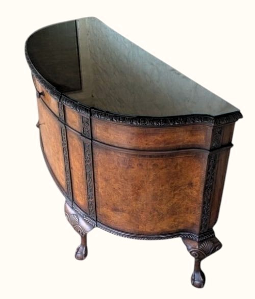 A semicircular burr walnut demi-lune sideboard featuring carved cabriole legs with ball-and-claw feet and decorative foliage carvings on the upright pilasters. View VII