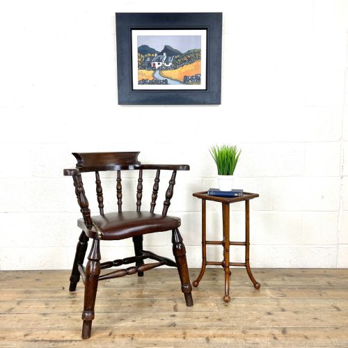 fig 1. An antique dark brown wooden smokers bow armchair featuring turned spindles, a curved top rail, and a brown leather upholstered seat secured with brass studs.
