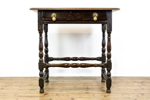 fig 1. A dark elm side table featuring turned legs, horizontal turned stretchers, and a single drawer with brass drop handles.