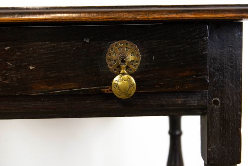 fig 2. A dark elm side table featuring turned legs, horizontal turned stretchers, and a single drawer with brass drop handles.