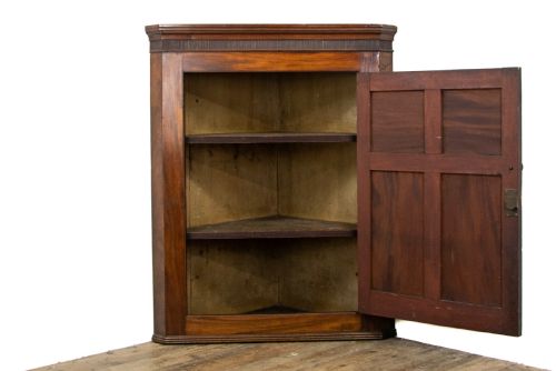fig 1. An antique mahogany corner cupboard featuring a single door with four raised flame mahogany panels, a fluted cornice, and brass hardware.