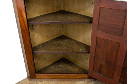 fig 2. An antique mahogany corner cupboard featuring a single door with four raised flame mahogany panels, a fluted cornice, and brass hardware.