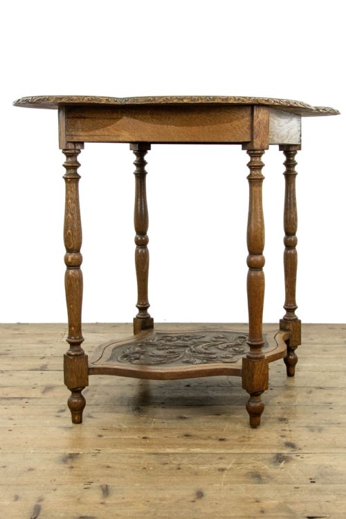 fig 1. A carved oak side table featuring a lobed, relief-carved top with floral motifs, four turned legs, and a carved lower tier shelf.