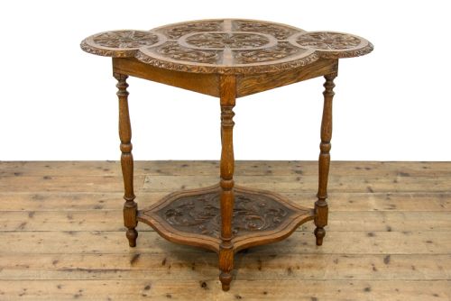 fig 2. A carved oak side table featuring a lobed, relief-carved top with floral motifs, four turned legs, and a carved lower tier shelf.