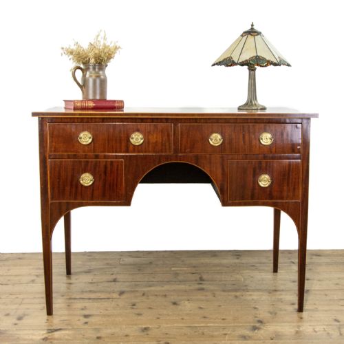 fig 1. An antique Sheraton Revival mahogany side table featuring four drawers, string inlay detailing, brass ring handles, and an arched central kneehole on tapered square legs.