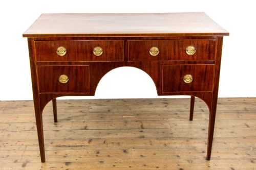 fig 2. An antique Sheraton Revival mahogany side table featuring four drawers, string inlay detailing, brass ring handles, and an arched central kneehole on tapered square legs.