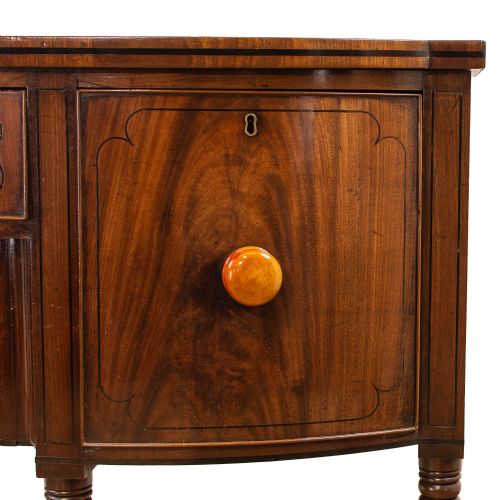 fig 1. An antique mahogany bow-front sideboard featuring turned reeded legs, central drawers, and flanking cupboard doors with turned wooden knobs.