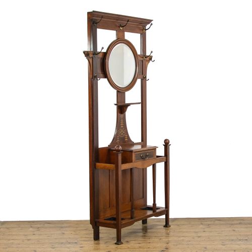 fig 2. An Edwardian mahogany hall stand featuring a central circular mirror, marquetry inlay, brass coat hooks, a single drawer, and umbrella holders with drip trays.