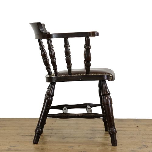 fig 1. A dark wood antique smokers bow armchair featuring turned spindles, a curved crest rail, and a brown leather seat with brass studs.