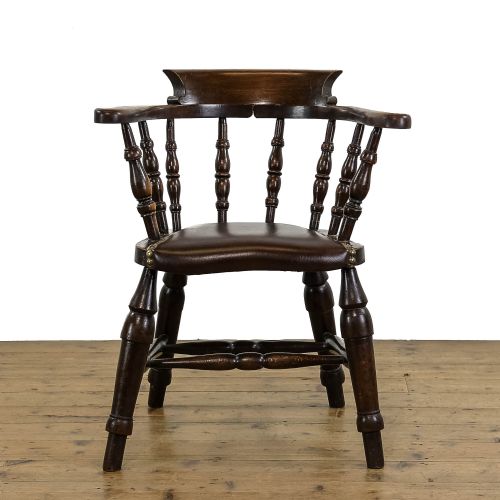 fig 2. A dark wood antique smokers bow armchair featuring turned spindles, a curved crest rail, and a brown leather seat with brass studs.