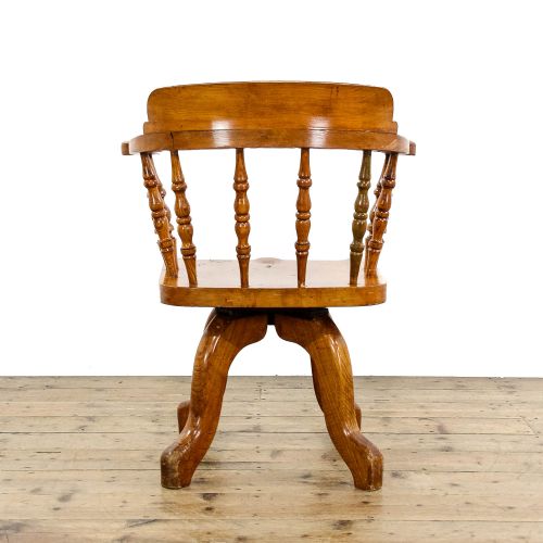 fig 1. An early twentieth-century wooden captains chair with turned spindles, a curved backrest, a solid saddle seat, and a swivel base.