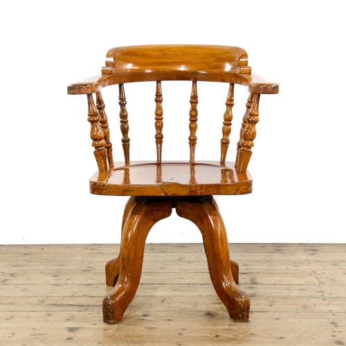fig 2. An early twentieth-century wooden captains chair with turned spindles, a curved backrest, a solid saddle seat, and a swivel base.