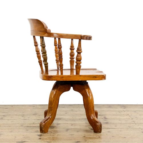 fig 3. An early twentieth-century wooden captains chair with turned spindles, a curved backrest, a solid saddle seat, and a swivel base.