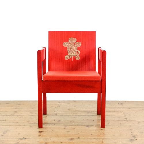 fig 1. A mid-century modern vermilion red wooden armchair featuring a flat square backrest printed with a gold Prince of Wales crest.
